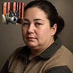 A majestic dog with thick fur poses calmly against a backdrop of vibrant autumn leaves seen through vertical wooden slats, creating a warm and cozy fall atmosphere.