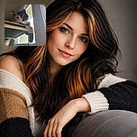 A curious calico cat lounges on a raised hammock-style perch by a window, peering down with wide, inquisitive eyes as if plotting a grand adventure or just judging your life choices.