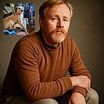 A scruffy, light brown dog lounges comfortably on a couch covered with colorful blankets and cushions, gazing thoughtfully off to the side. The cozy indoor setting includes a wooden floor, a shelf with framed photos, a whimsical wooden cat sculpture, and a pot with a colorful pinwheel, creating a warm and charming atmosphere.