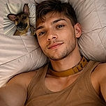 A close-up photo of a relaxed dog lying on a rumpled light-colored blanket, looking up with big ears flopped out and curious eyes, capturing a cozy and intimate moment.
