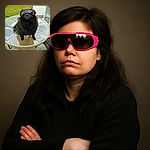 A fluffy black dog wearing oversized pink sunglasses sits confidently on a glass-top outdoor table, looking like the coolest canine in town ready to block out the haters and the sun.