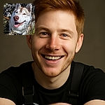 A happy husky dog with a big smile is lounging in the grass surrounded by some rocks and greenery, basking in the sunlight with a playful and content expression.