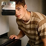 A curious tabby cat peers into a fridge, seemingly plotting its next snack heist amidst ice cream, coffee, and frozen goodies. The fridge light casts a soft glow on the feline's focused face, capturing a classic moment of pet mischief.