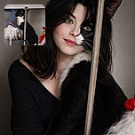 A curious black and white cat peeks out from behind a vertical pole, partially hidden among festive gnome decorations, creating a whimsical and slightly mysterious scene.