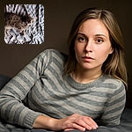 A cozy tabby cat with striking green eyes lounges comfortably on a wrinkled, striped bedspread, casting a curious glance at the camera as if pondering the mysteries of the universe—or just wondering where the next meal is.