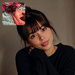A wide-eyed black kitten sticks out its tiny pink tongue while being cuddled like a fuzzy little celebrity, nestled in colorful blankets with an impressively dramatic bedspread backdrop.
