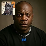 A close-up photo of a large black dog with soulful brown eyes sitting on a tiled kitchen floor, looking up with a slightly sad expression, framed by wooden cabinets and a stainless steel oven in the background.
