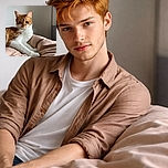 A regal ginger and white cat lounges elegantly on a soft, beige blanket, its eyes half-closed in a look of calm contentment. The soft natural light highlights the cat's fur texture, while the muted background keeps the focus on this feline royalty.