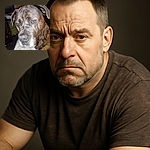 A close-up photo of a large brindle dog with soulful amber eyes, looking slightly downcast or contemplative. The background is cluttered with household items, giving a casual, unpolished snapshot vibe.