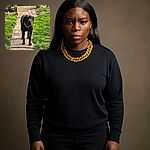 A regal black dog wearing a chunky gold chain stands confidently on a garden path, surrounded by lush green grass and a colorful flower pot in the background, basking in the soft sunlight.