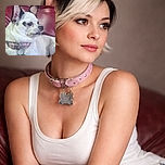 A small white and black dog with large ears lounges on a red leather couch, looking off to the side with a calm expression. The dog wears a pink collar with a blue bone-shaped tag. White text overlay humorously praises the dog, adding a playful tone to the cozy scene.