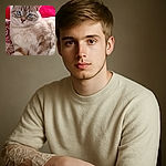 A fluffy cat with striking blue eyes lounges comfortably on a patterned pink and red fabric, looking directly at the camera with an expression that says, 'Yes, I am the ruler of this couch.'