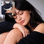 A peaceful black and white cat is snoozing comfortably with its head resting on a person's knee, radiating pure relaxation and trust in a cozy indoor setting.