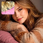 A fluffy cat lounges on a pink cushion with a slightly grumpy yet adorable expression, surrounded by cozy fabrics and a worn leather surface beneath, basking in soft natural light.