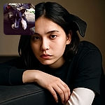 A cozy dog lounges on a couch, its head resting on the edge with one paw stretched out, looking relaxed and a bit contemplative in soft indoor lighting.