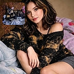 A striking tortoiseshell cat lounges regally on a pile of cozy blankets against an ornate patterned couch, eyes wide open as if guarding its plush kingdom with fierce curiosity.