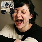 A fluffy black and white cat caught mid-yawn or meow, looking adorably goofy with its mouth open wide. The background features a cozy cat tree and window blinds letting in soft natural light, making the scene feel warm and homey.