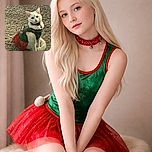 A charming white cat dressed in a festive green and red outfit sits gracefully on a plush beige carpet, looking curiously at the camera with a slightly tilted head, as if ready for holiday mischief.