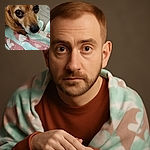 A close-up photo of a small dog with big, expressive eyes looking up with an innocent and slightly worried expression. The dog is sitting on a colorful blanket with pastel shades of pink, blue, and white, featuring heart and leaf patterns. The background includes a wooden floor, adding a cozy indoor vibe.