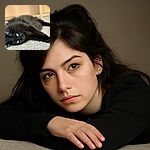A fluffy black cat lounges on a textured carpet, its piercing yellow eyes staring directly at the camera with a mysterious and regal gaze. The soft focus background highlights the cat's sleek fur and relaxed posture, making it look like the ultimate nap champion.