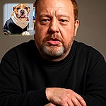 A charming bulldog dressed in a sporty black Adidas jacket sits attentively indoors, eyeing a well-used baseball on the tiled floor, ready for a game or a playful fetch session.