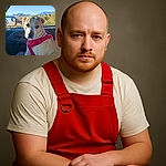 A charming dog wearing a bright red harness sits patiently in the passenger seat of a car, gazing thoughtfully at the camera. The window reveals a scenic backdrop of mountains and greenery under a clear blue sky, adding a serene outdoor vibe to this cozy car moment.
