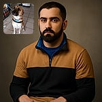 A well-behaved dog wearing a blue collar and harness sits patiently on a tiled floor indoors, looking slightly upwards with a calm and attentive expression. The background includes a coat stand, a litter box, and several bottles of soda lined up against the wall.