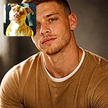A close-up photo of a brown and white dog with a serious expression, sitting in a spot of sunlight that highlights its face and chest against a dark background.