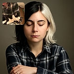 A cozy scene where a black and white cat is peacefully napping on a person's arm, who is wearing a plaid shirt. The cat looks completely relaxed, with its eyes closed and a soft pink nose, while the person smiles gently, creating a warm, comforting atmosphere.