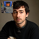 A curious black and white dog with a collar tags along the bottom left corner, gazing slightly off camera. Behind, a cozy wood-burning stove blazes warmly, framed by a vibrant blue wall and stacked firewood, creating a snug and inviting atmosphere.