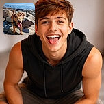 A happy dog with big, gleaming eyes and tongue out is standing on rocky terrain near the ocean, looking like it's ready for an adventure or a game of fetch with the waves.