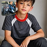 A charming photo capturing a young child in a car seat gently holding the chin of a curious gray puppy with a red collar, both seated in the backseat of a vehicle. The child looks thoughtfully at the puppy, creating a sweet and heartwarming moment. The background shows the car window with a glimpse of the outside scenery.