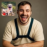 A cheerful dog with a big smile, sitting on a dirt path surrounded by green grass and plants, wearing a harness and leash. A large red heart emoji covers part of the dog's body, adding a playful and loving touch to the photo.