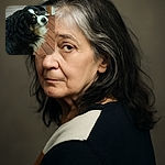 A fluffy black and white dog with a curious expression looks back over its shoulder on a wooden floor indoors, with a slightly blurry effect giving a sense of motion or quick head turn.