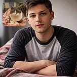 A chubby gray and white cat is comfortably lounging on a cozy plaid blanket, staring serenely at the camera with a slightly grumpy expression, surrounded by a softly lit bedroom setting.