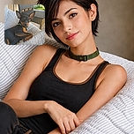 A charming black and tan dog lounges comfortably on a striped cushion, gazing curiously at the camera with big, expressive ears standing tall. Behind, a woven chair and a sunny garden add a cozy outdoor vibe to the scene.