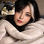 A cozy tuxedo cat wrapped snugly in a soft blanket, looking relaxed and slightly curious with its whiskers and ears sharply in focus against a softly blurred bedroom background.