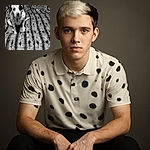 A blurry black and white photo of a spotted dog sitting on a textured blanket with patterned pillows in the background. The dog's face is out of focus, making it look like it's in motion or shaking its head.