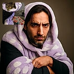 A cozy cat peeks out from a fluffy purple and white towel, looking a bit like a tiny tiger wrapped in a soft cocoon. The colorful blanket in the background adds a splash of fun to this snug indoor scene.