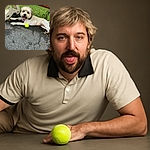 A fluffy dog is lying on a paved surface next to a tennis ball, tongue out and looking happily tired, with a green grassy background behind a chain-link fence and a wooden beam overhead.