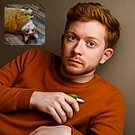 A charming ginger and white cat lies on its back on a wooden floor, clutching a green plush toy with a tag. The cat's wide eyes are looking directly at the camera, giving an innocent and playful vibe.
