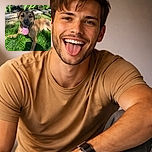 A happy dog lounging on vibrant green grass with its tongue playfully sticking out, basking in the warm sunlight with a garden backdrop of leafy plants and a stone border.