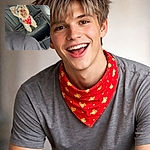 A tiny, ecstatic Yorkshire Terrier wearing a festive red bandana sits proudly on a leather car backseat, tongue out and eyes sparkling like it just told a hilarious joke. The pup's fluff and perky ears steal the show while the car interior provides a sleek, monochrome backdrop — a perfect smug-road-trip vibe.
