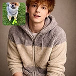 A fluffy Pomeranian stands on lush green grass with a curious expression, its little tongue peeking out as it poses next to a neat pile of bright yellow tennis balls, ready for a playful game.