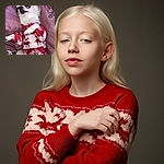 A small white dog dressed in a cozy red and white holiday sweater lies comfortably on a purple blanket. The dog looks relaxed with a slightly amused expression, as if posing for a festive photo. The image has Snapchat interface elements overlaid, including text and icons.