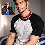 A handsome black and white dog with a red collar poses on a bed covered with a blue and white blanket. The background shows a dog crate filled with toys and tissues on top. Bright pink text above the dog reads 'MY HANDSOME BOY,' adding a playful and affectionate touch to the cozy indoor scene.