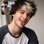 A blurry close-up of a fluffy white and gray cat with its mouth open, possibly mid-meow or caught in an awkward expression, sitting in front of a wooden door with a window showing an out-of-focus outdoor scene.