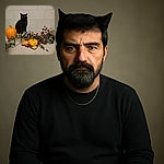 A poised black cat sits regally behind a fall-themed table arrangement featuring pumpkins, colorful autumn leaves, and a rustic birdhouse, all set against a plain tiled wall backdrop.