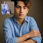A fluffy puppy is being lovingly held by a person in a blue striped shirt against a brick wall backdrop. The puppy's paws are prominently displayed, making it look ready for a high-five or a paw shake.