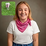 A happy golden retriever puppy wearing a bright pink bandana stands cheerfully on a lush green lawn dotted with small flowers, looking straight at the camera with an open-mouthed smile.